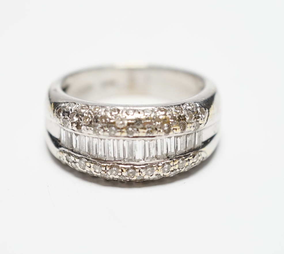 A modern 750 white metal and graduated baguette cut diamond set half hoop ring, with diamond chip set borders, size N, gross weight 9.3 grams.
